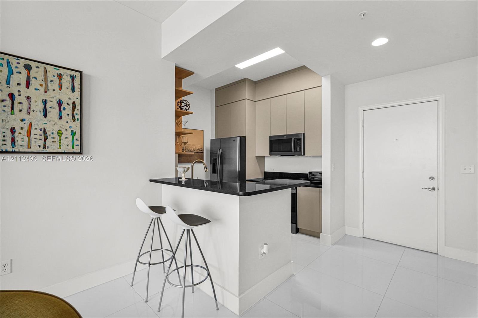 Kitchen featuring a breakfast bar with stone-surfaced countertop, integrated flat-panel cabinetry, built-in microwave, and large-format tile flooring