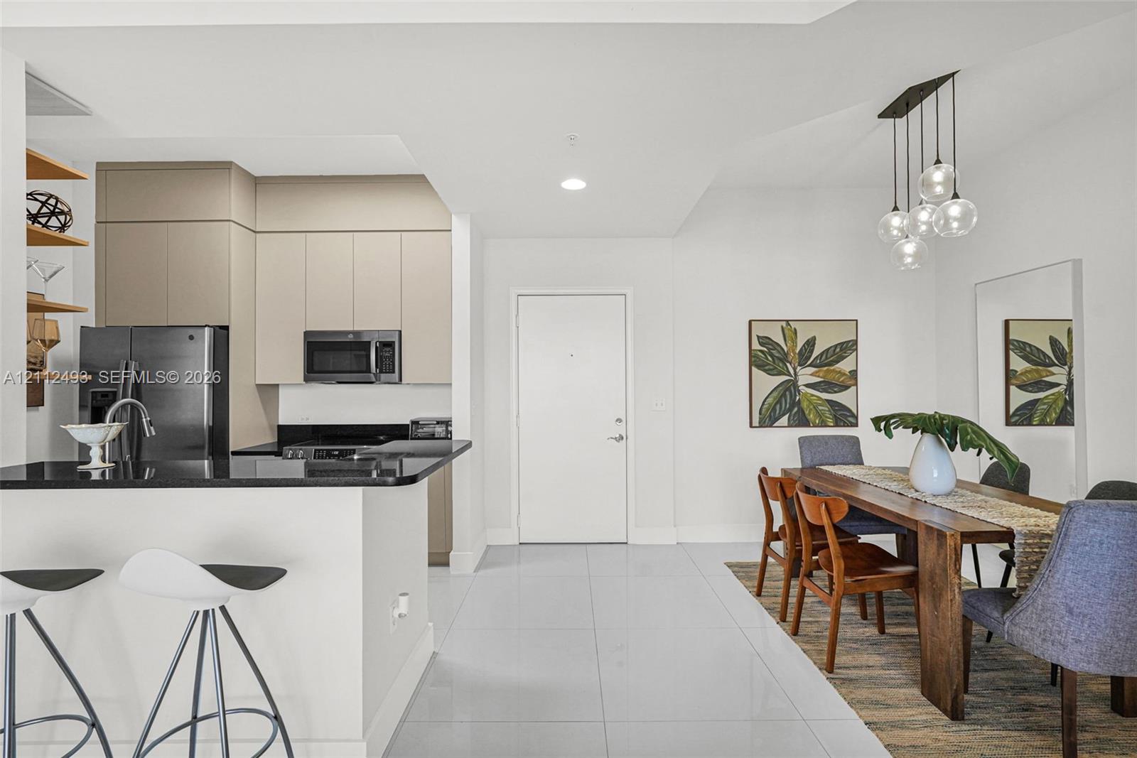 Kitchen featuring flat-panel cabinetry, a black countertop breakfast bar, built-in stainless steel appliances, large-format tile flooring, and multi-globe pendant lighting