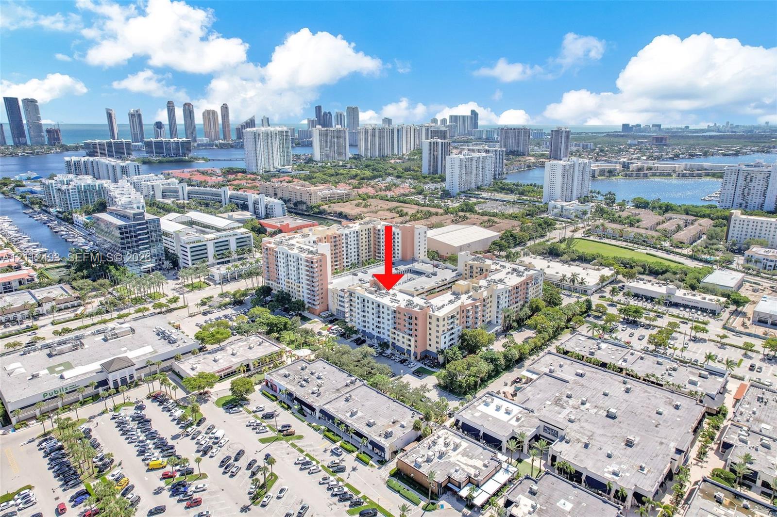 Aerial perspective of a multi-story residential building featuring a light-colored facade, flat roof structure, and surrounding urban infrastructure