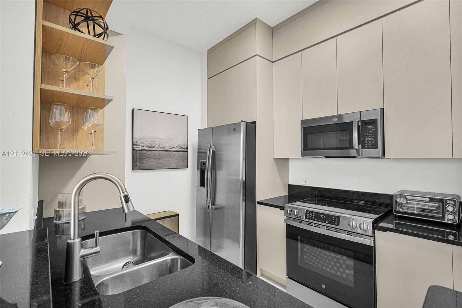 Kitchen featuring full-height flat-panel cabinetry, dark stone countertops, stainless steel appliances, and integrated wood-finish open shelving