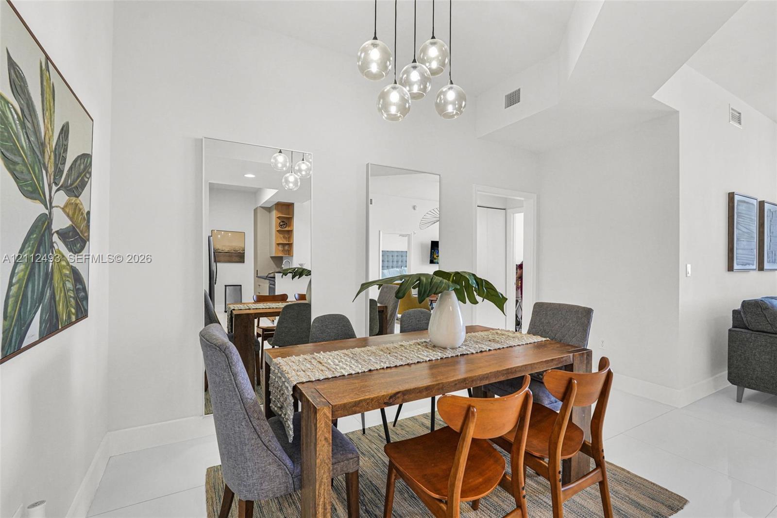 High-ceiling interior featuring a multi-globe pendant light fixture, dual floor-to-ceiling wall mirrors, and large-format tile flooring
