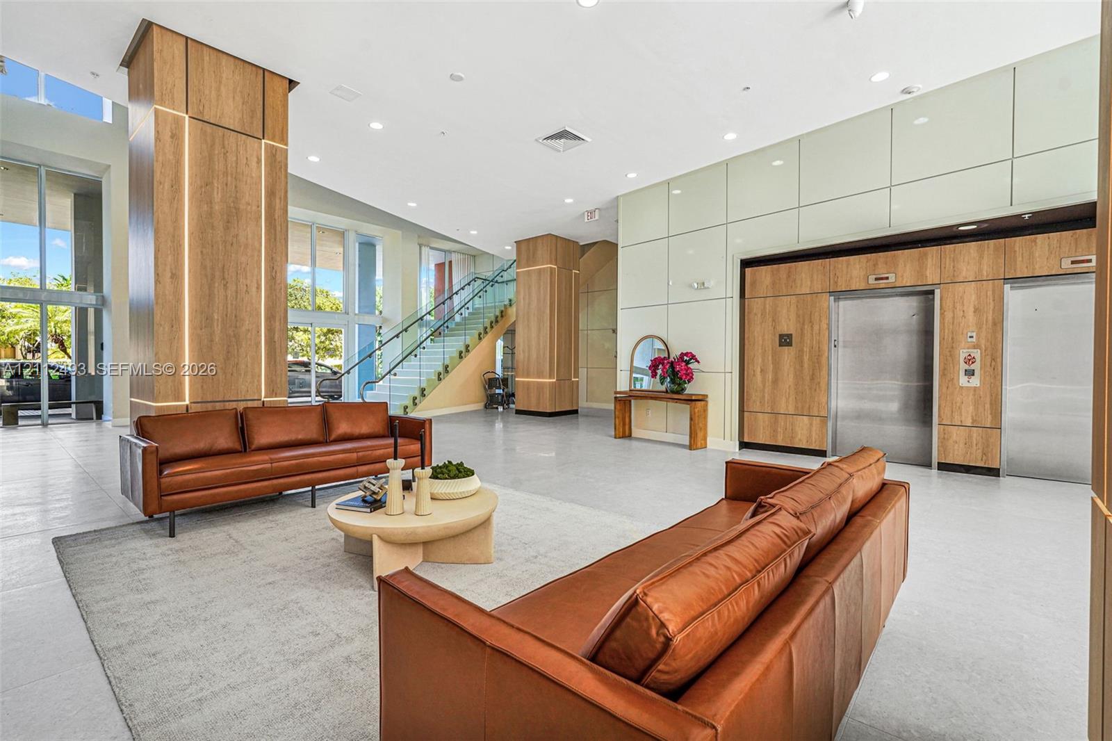 Grand lobby featuring floor-to-ceiling wood-finish pillar detailing, polished tile flooring, a glass-panel staircase, and dual stainless steel elevators Grand lobby featuring floor-to-ceiling wood-finish pillar detailing, polished tile flooring, a glass-panel staircase, and dual stainless steel elevators