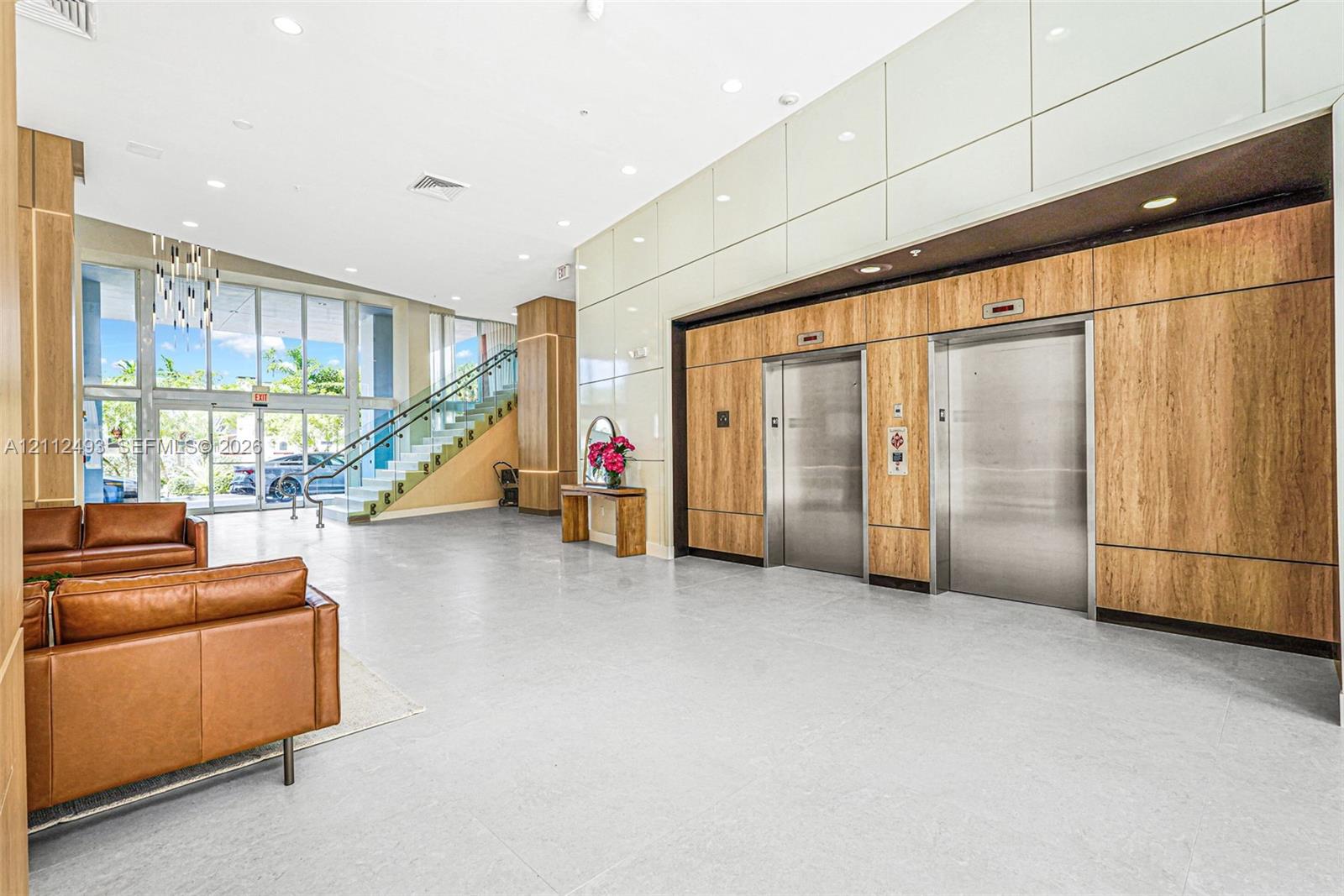 Expansive lobby featuring light-toned tile flooring, floor-to-ceiling wood-finish wall paneling, dual stainless steel elevators, and floor-to-ceiling glass windows with a staircase Expansive lobby featuring light-toned tile flooring, floor-to-ceiling wood-finish wall paneling, dual stainless steel elevators, and floor-to-ceiling glass windows with a staircase
