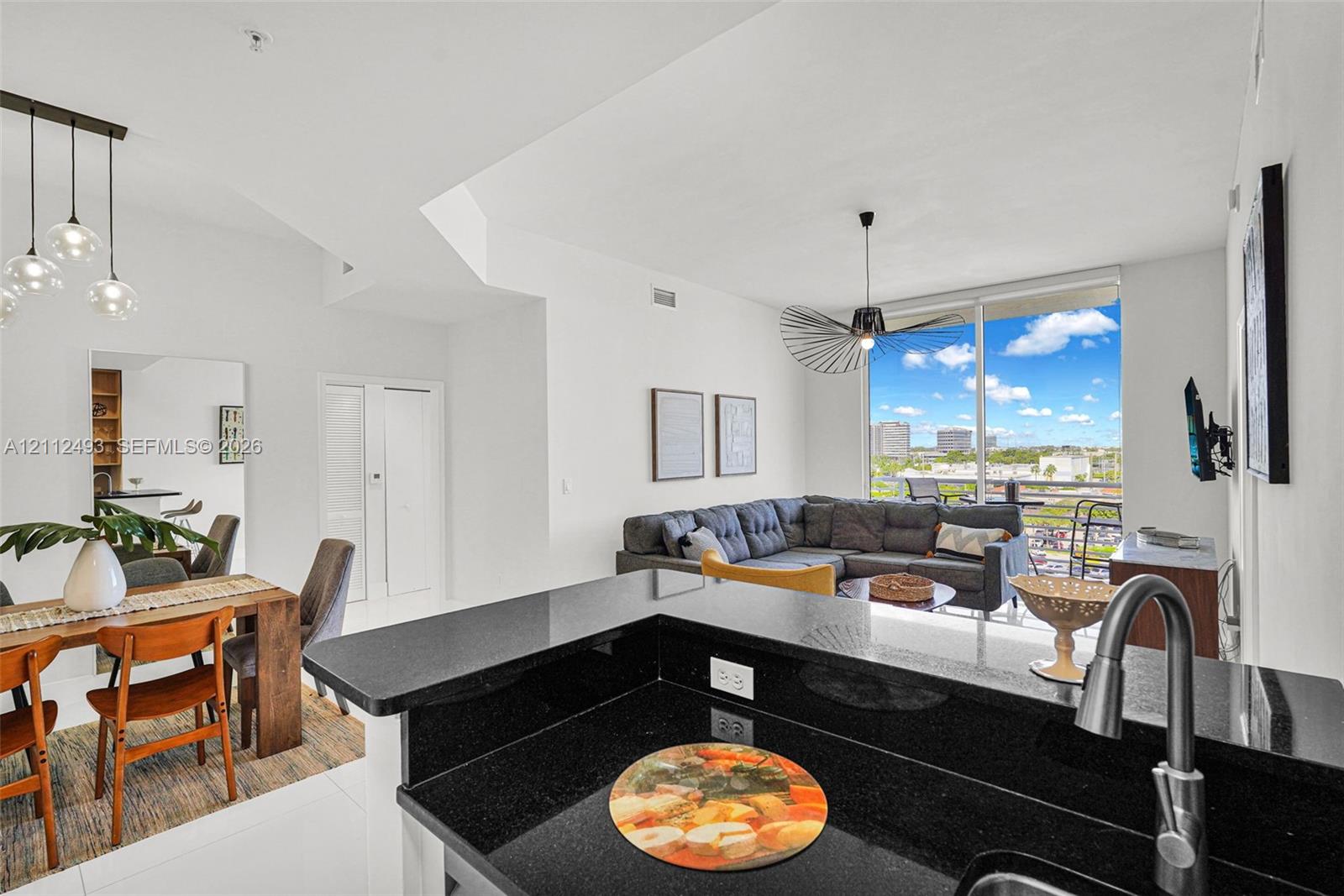 Open-concept interior featuring high-gloss flooring, dark stone countertops, modern pendant lighting, a designer ceiling fan, and floor-to-ceiling glass windows