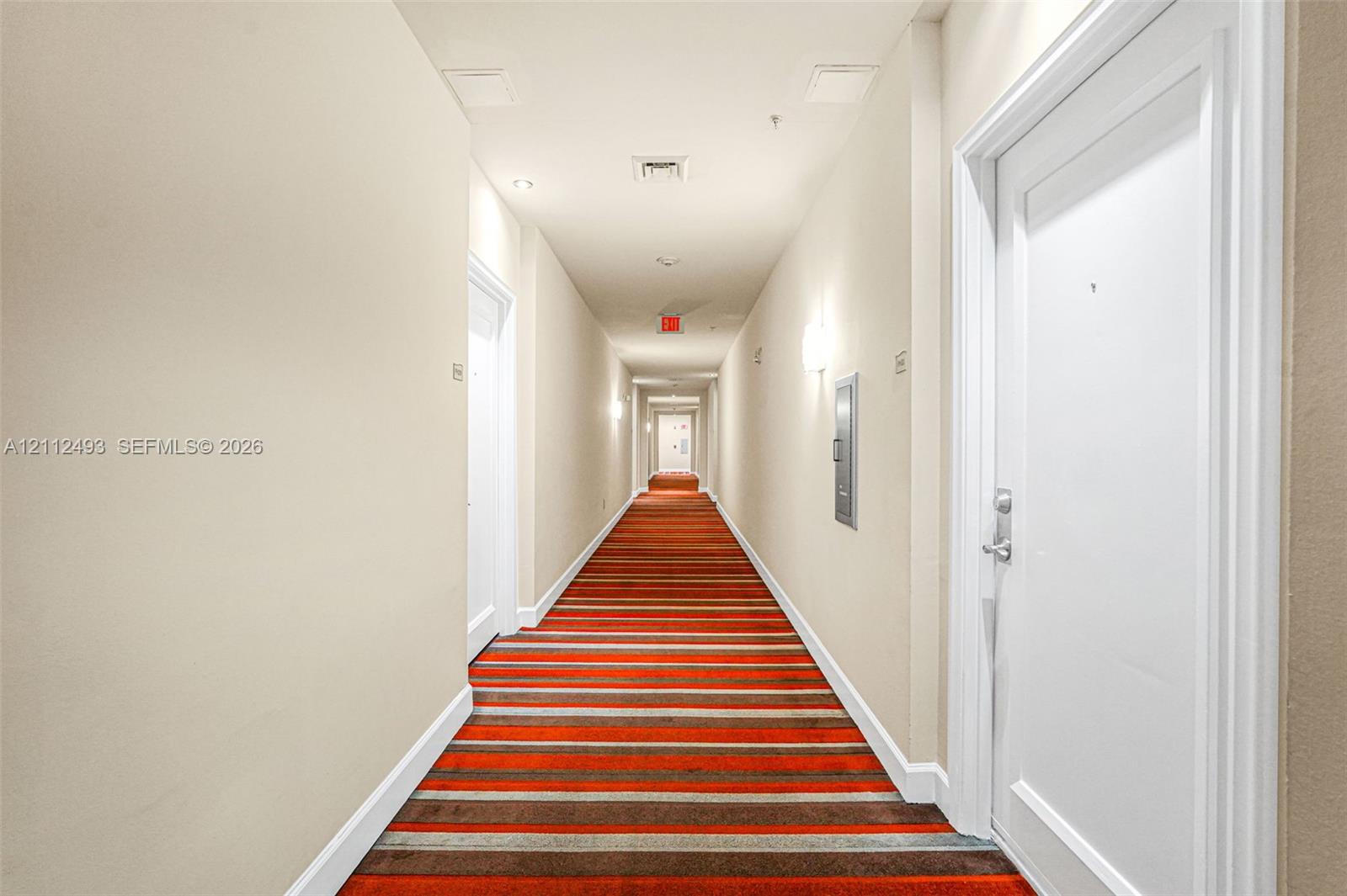 Interior hallway featuring striped carpeting, solid-core doors, and wall-mounted sconce lighting