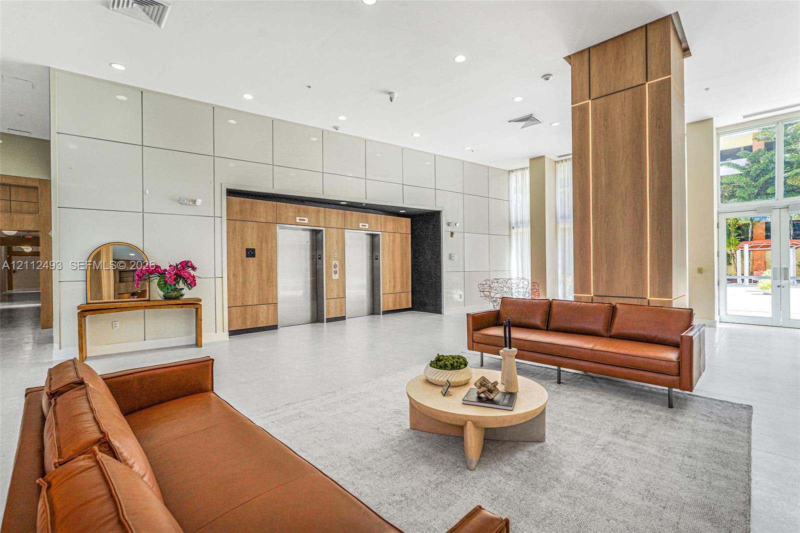 Lobby featuring panelized wall finishes, double elevator bank with wood-tone accents, recessed lighting, expansive glass entryway, and large-format flooring Lobby featuring panelized wall finishes, double elevator bank with wood-tone accents, recessed lighting, expansive glass entryway, and large-format flooring