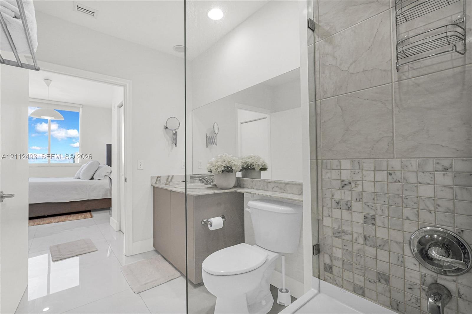 Bathroom featuring polished tile flooring, vanity with stone-finish countertop, full-width mirror, and shower enclosure with decorative stone-tile inlay