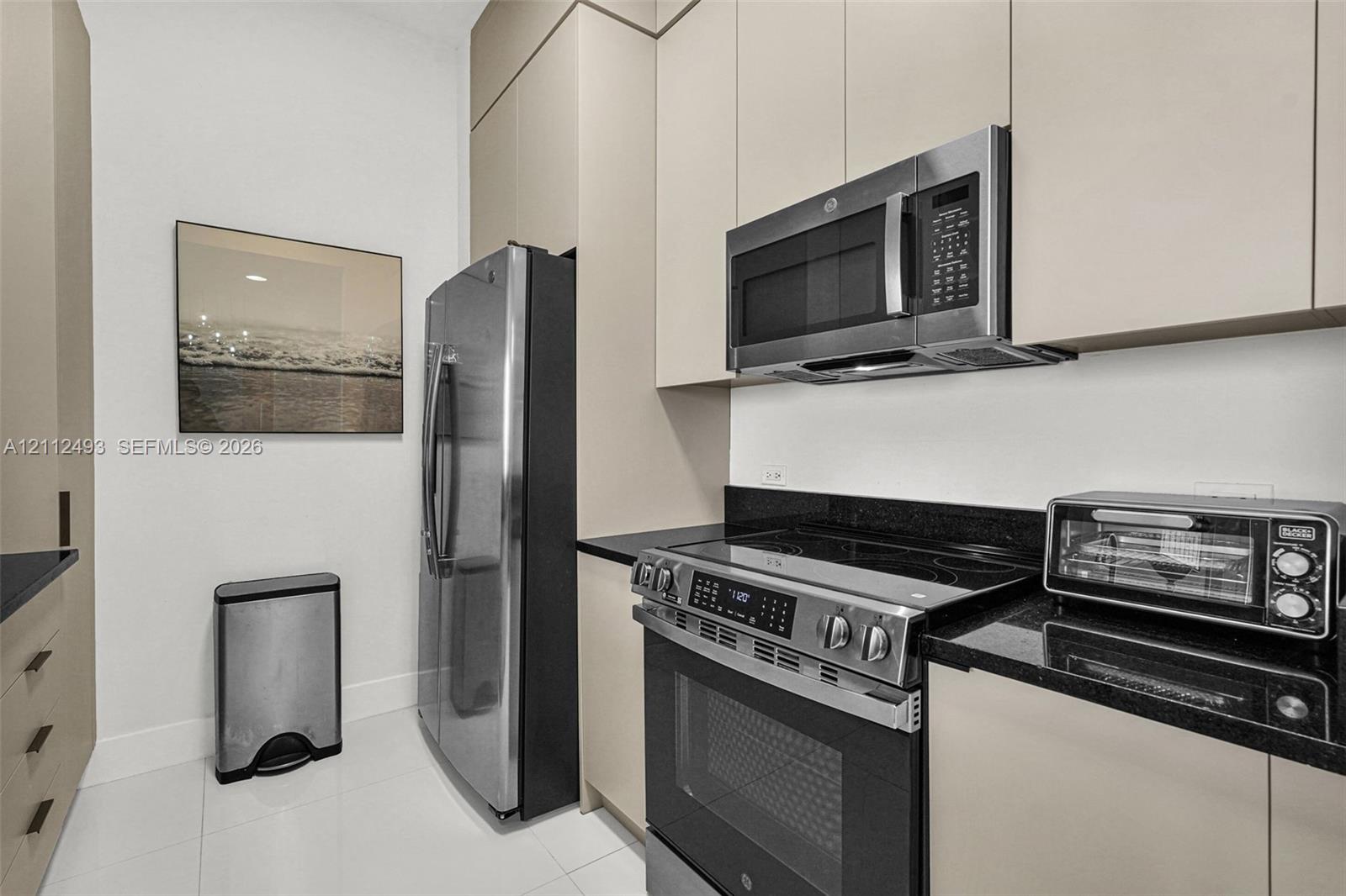 Flat-panel cabinetry in a neutral finish with black hardware, stone countertops, and stainless steel appliances including a convection range and over-the-range microwave