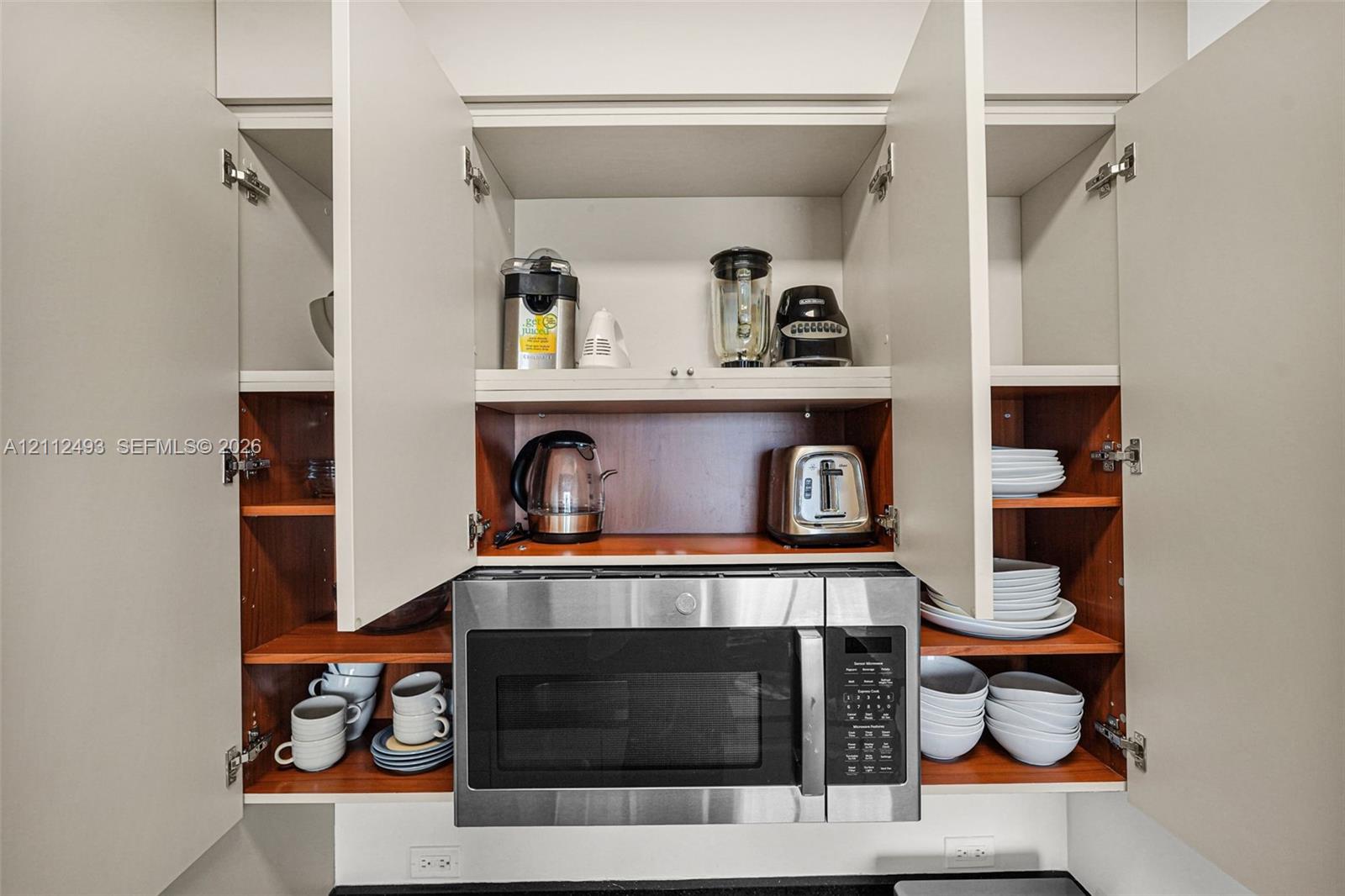 Built-in cabinetry featuring light-toned doors, open shelving, and a stainless steel integrated microwave