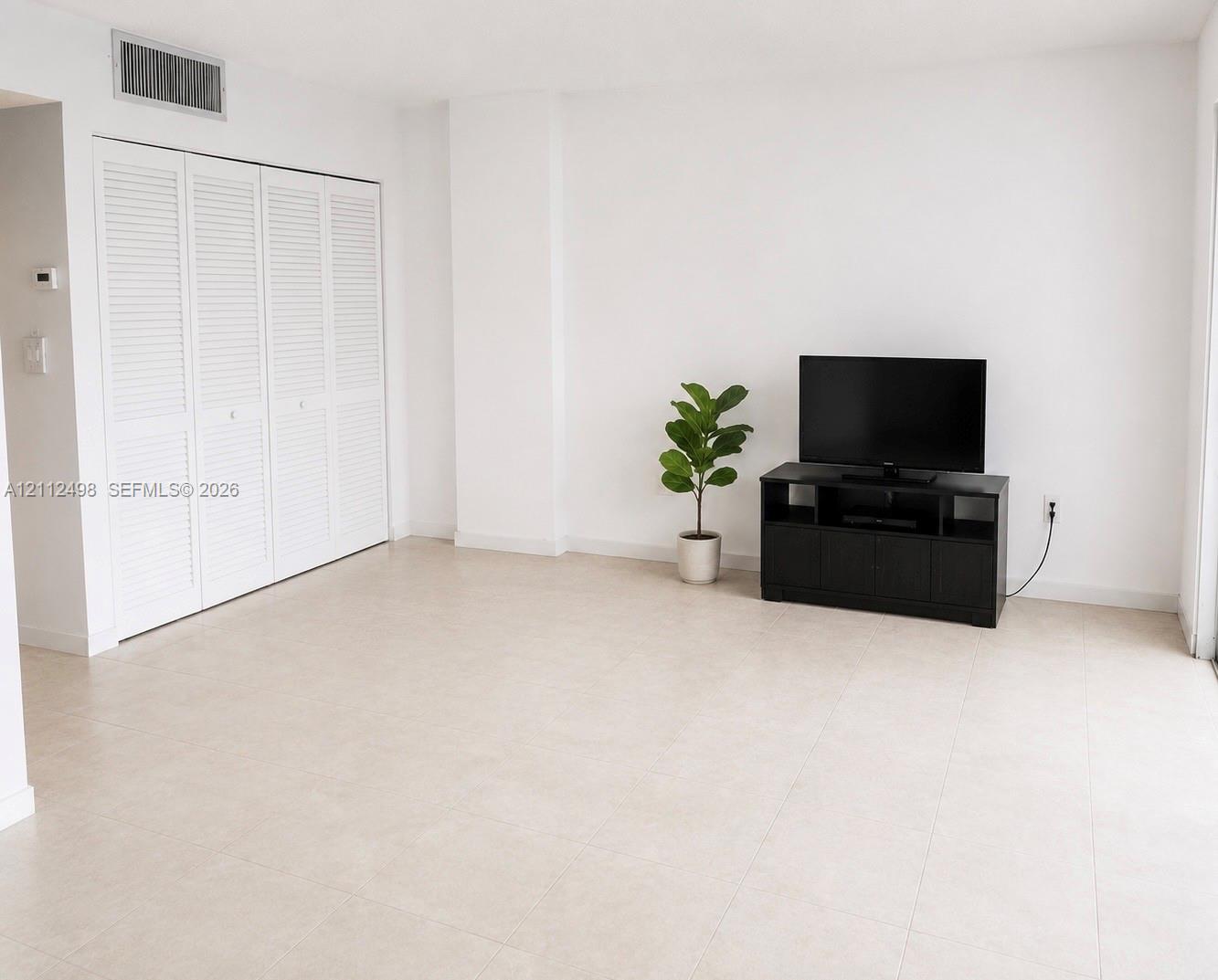 Light-toned tile flooring throughout with full-height closet featuring white louvered bifold doors