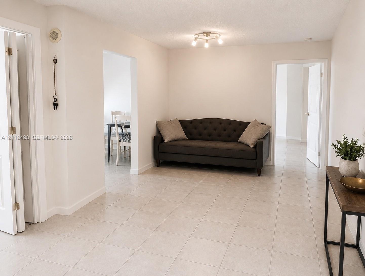 Neutral interior space featuring large-format ceramic floor tiling, crisp white walls, and a multi-directional brushed metal flush-mount light fixture