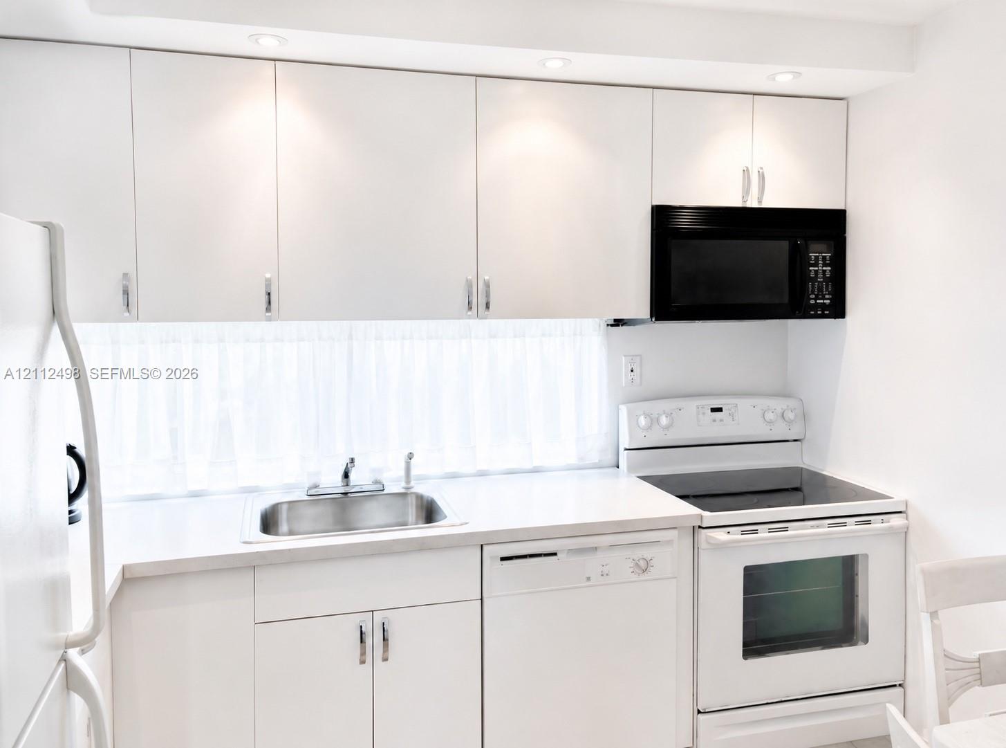 Kitchen featuring white cabinetry, solid-surface countertops, a stainless steel undermount sink, integrated dishwasher, and built-in recessed lighting