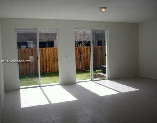 Living area featuring tile flooring, neutral wall tones, and dual sliding glass doors providing outdoor access