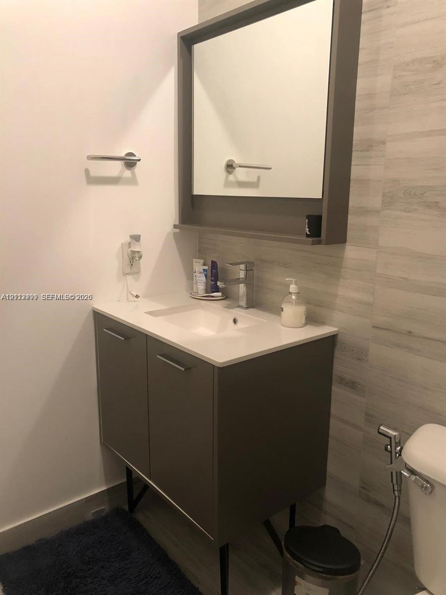 Vanity with a solid surface countertop, integrated sink, and metallic faucet, paired with a matching wall-mounted medicine cabinet and horizontal tile backsplash