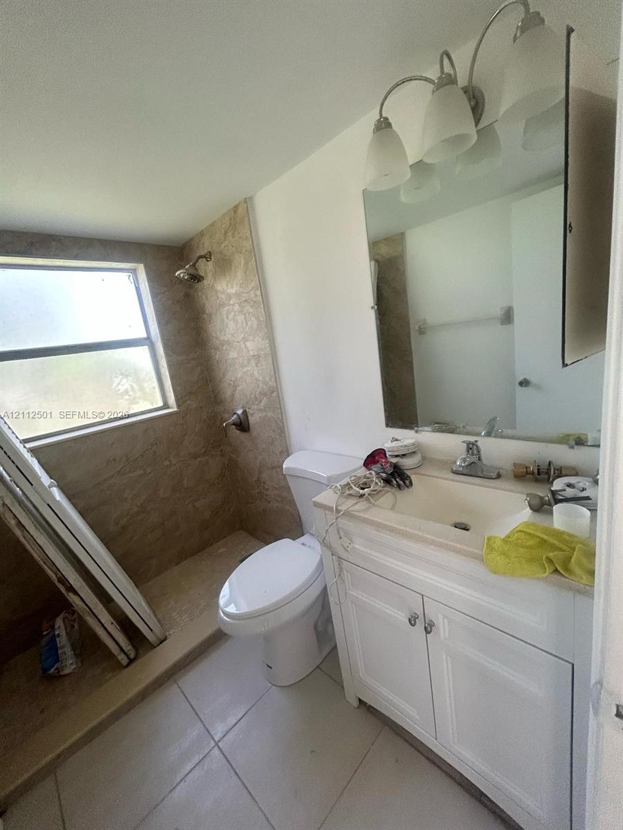 Bathroom featuring a white vanity cabinet with a solid surface countertop, an integrated sink with a chrome faucet, a three-light wall-mounted fixture, and a tile-surround shower Bathroom featuring a white vanity cabinet with a solid surface countertop, an integrated sink with a chrome faucet, a three-light wall-mounted fixture, and a tile-surround shower