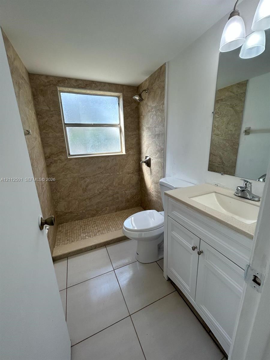 Bathroom featuring a white vanity with integrated basin, light-toned countertop, floor-to-ceiling textured tile shower surround, mosaic tile shower flooring, and large-format tile flooring Bathroom featuring a white vanity with integrated basin, light-toned countertop, floor-to-ceiling textured tile shower surround, mosaic tile shower flooring, and large-format tile flooring