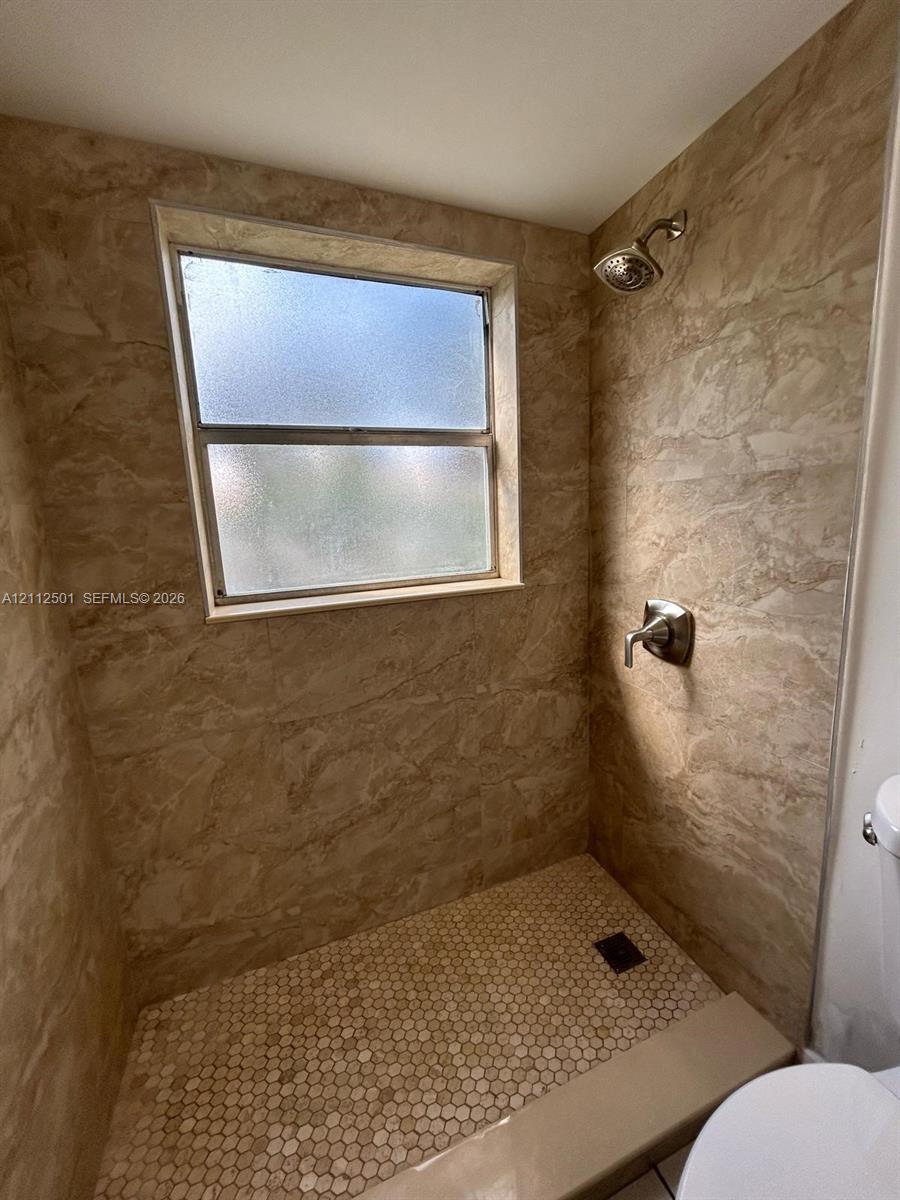 Walk-in shower featuring floor-to-ceiling large-format tile surround, hexagonal tile flooring, frosted glass window, and a single-handle polished metal shower fixture Walk-in shower featuring floor-to-ceiling large-format tile surround, hexagonal tile flooring, frosted glass window, and a single-handle polished metal shower fixture