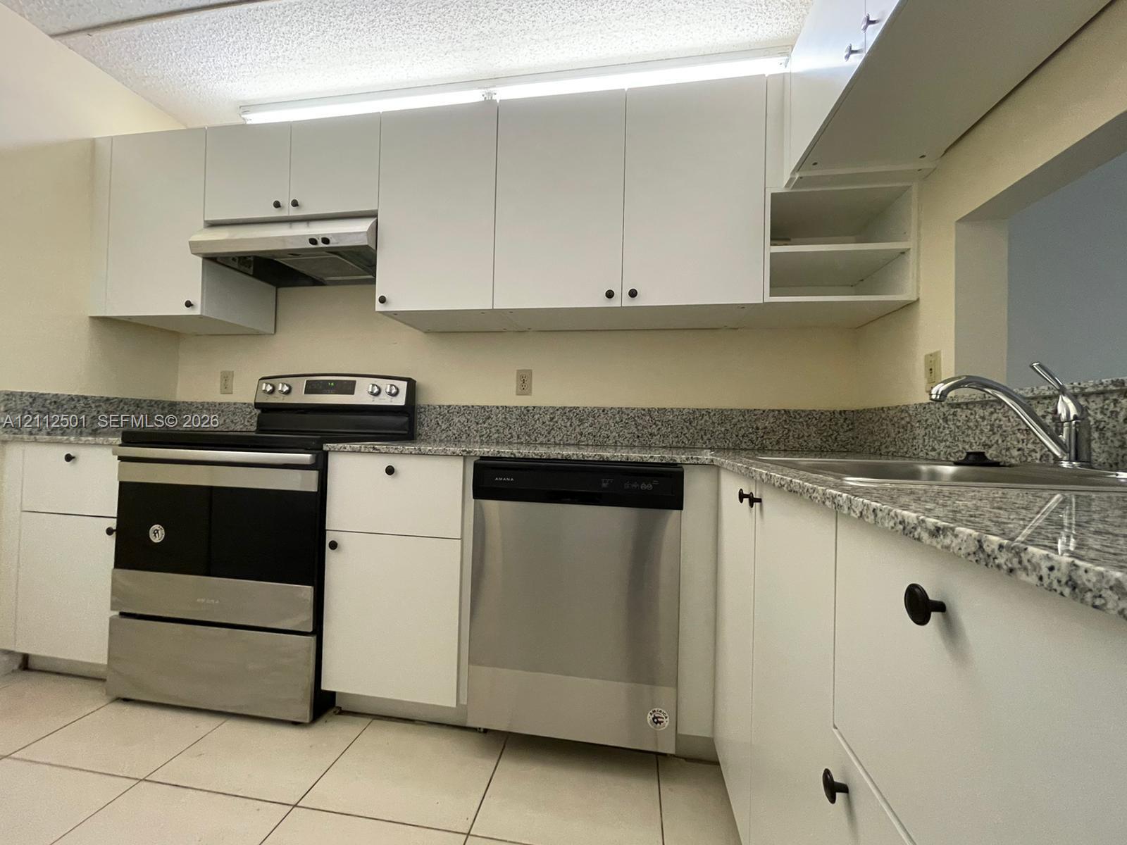 Kitchen featuring white cabinetry, stone-finish countertops, stainless steel appliances, and tile flooring