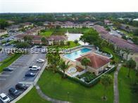Aerial perspective of a multi-unit property featuring a community swimming pool, spa, paved parking area, and manicured green spaces