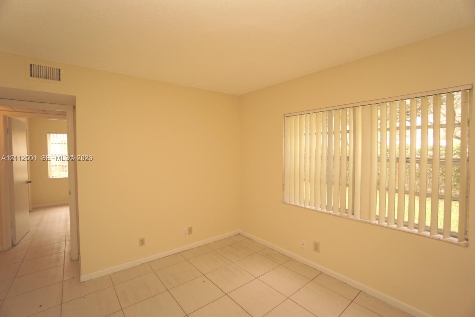 Interior space featuring light-toned tile flooring, neutral wall paint, and windows outfitted with vertical blinds