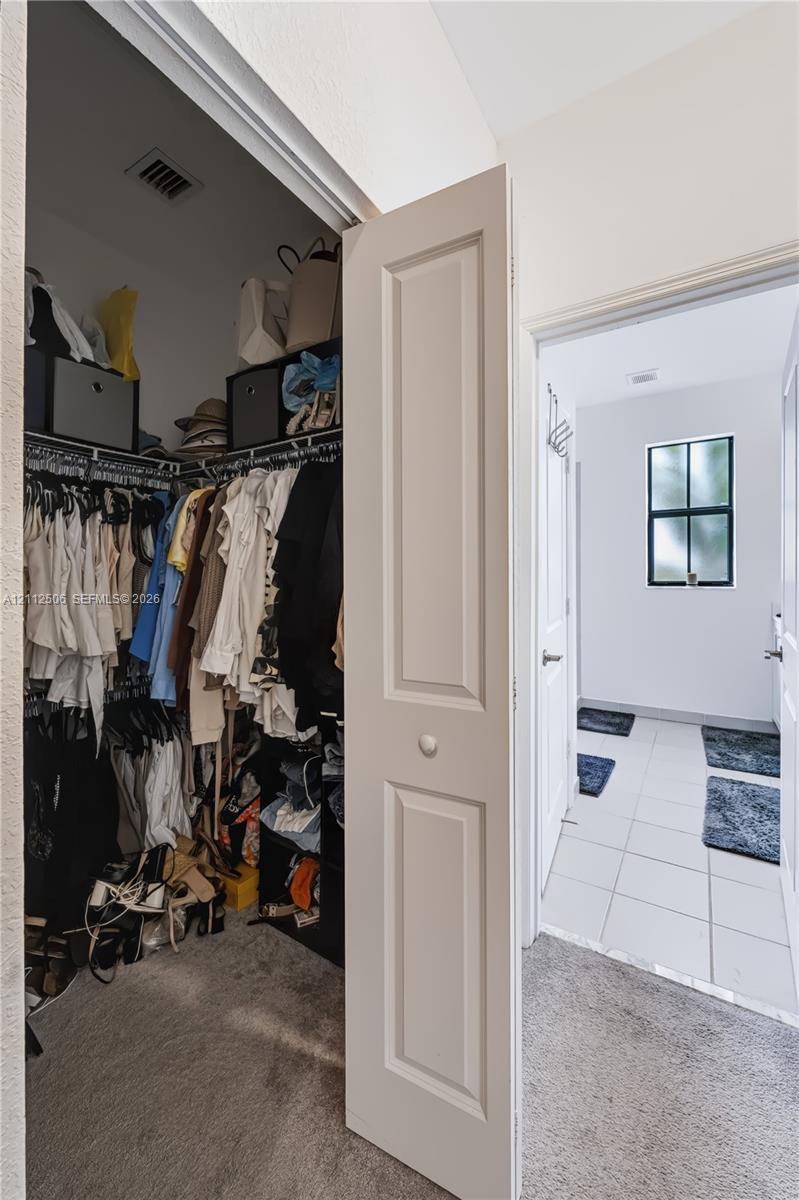 Walk-in closet featuring built-in wire shelving, paired with an entry area showcasing white tile flooring and a multi-pane window