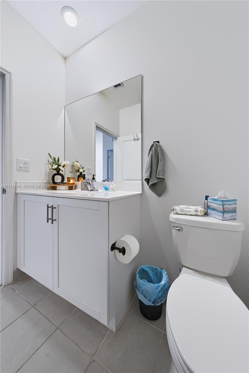 Shaker-style white vanity with stone-composite countertop, large wall-mounted mirror, matte black hardware, and neutral tile flooring