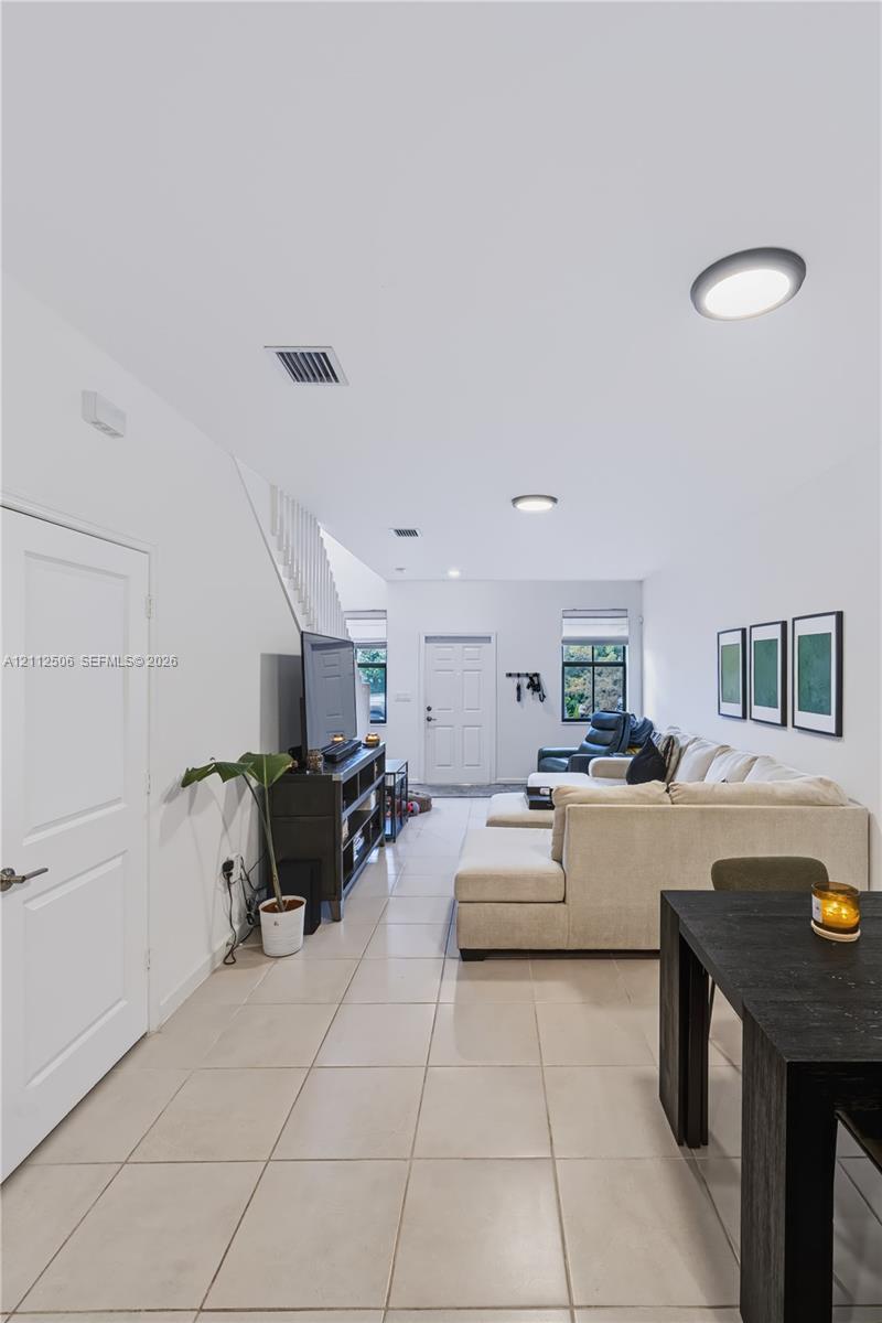 Open interior space featuring light-colored tile flooring, flush-mount circular lighting, and a white paneled entry door
