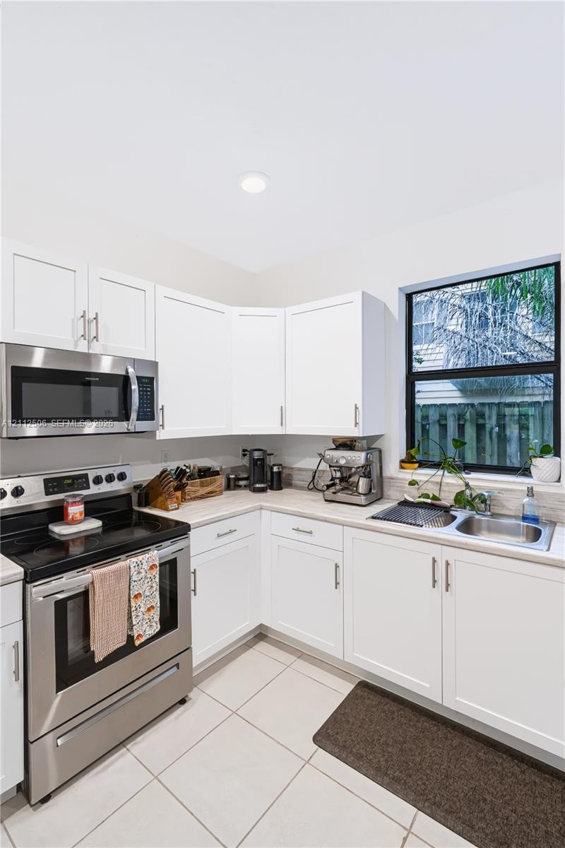 Kitchen featuring white shaker-style cabinetry, stainless steel appliances, neutral stone-finish countertops, tile flooring, and a single-basin undermount sink