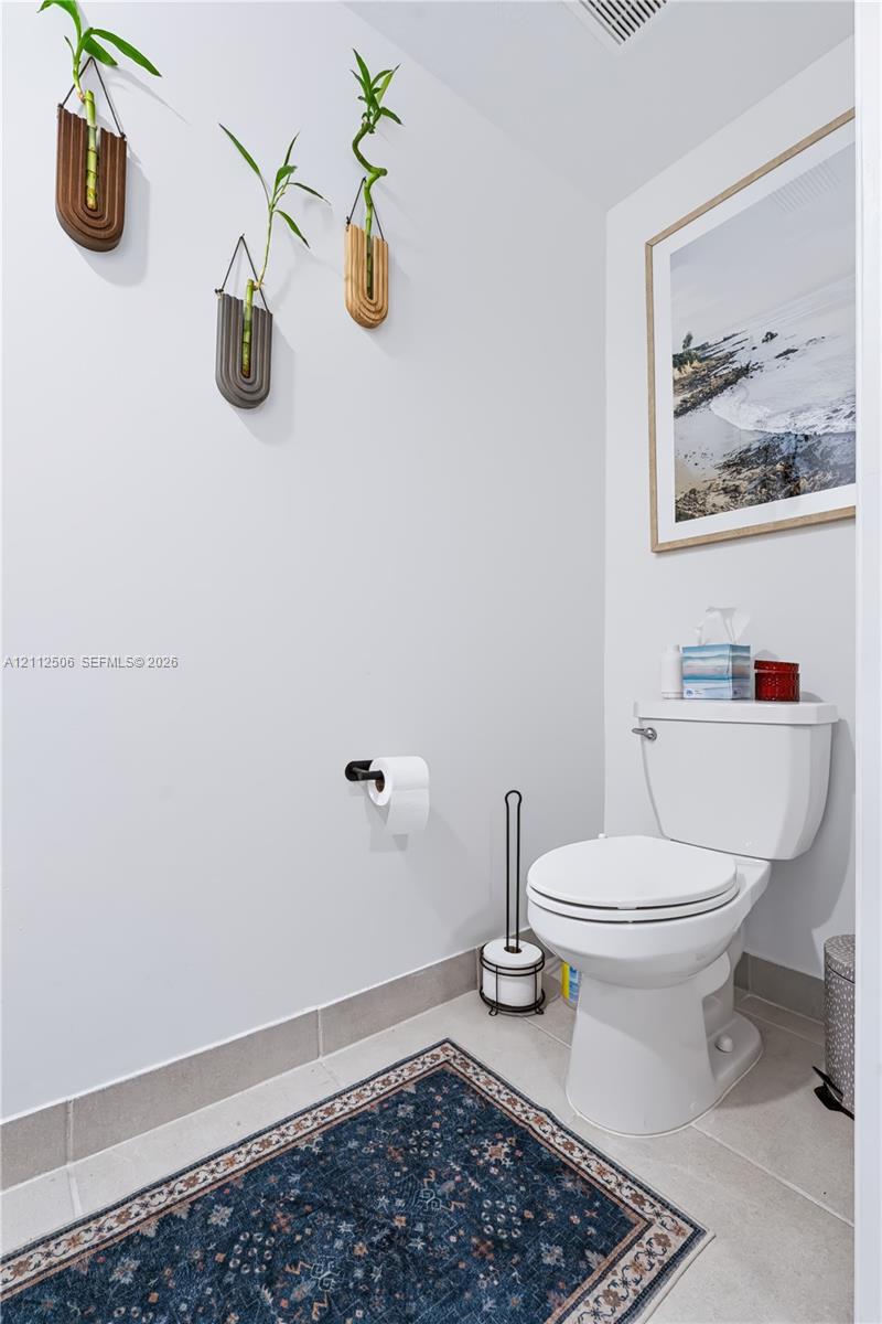 Neutral-toned restroom featuring a white porcelain commode, matte black wall-mounted toilet paper holder, and large-format tile flooring