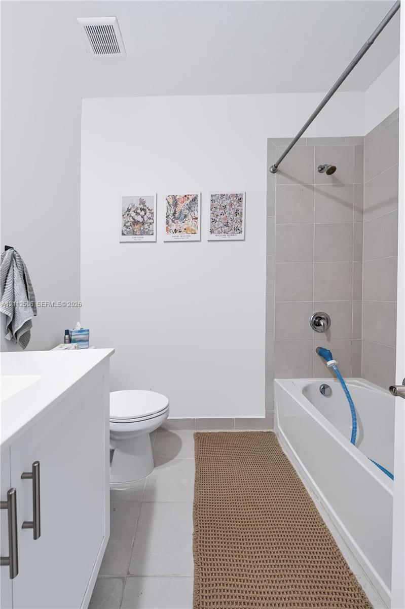Bathroom featuring a white vanity cabinet with metallic hardware, a white porcelain toilet, and a bathtub with neutral-toned wall tile surround