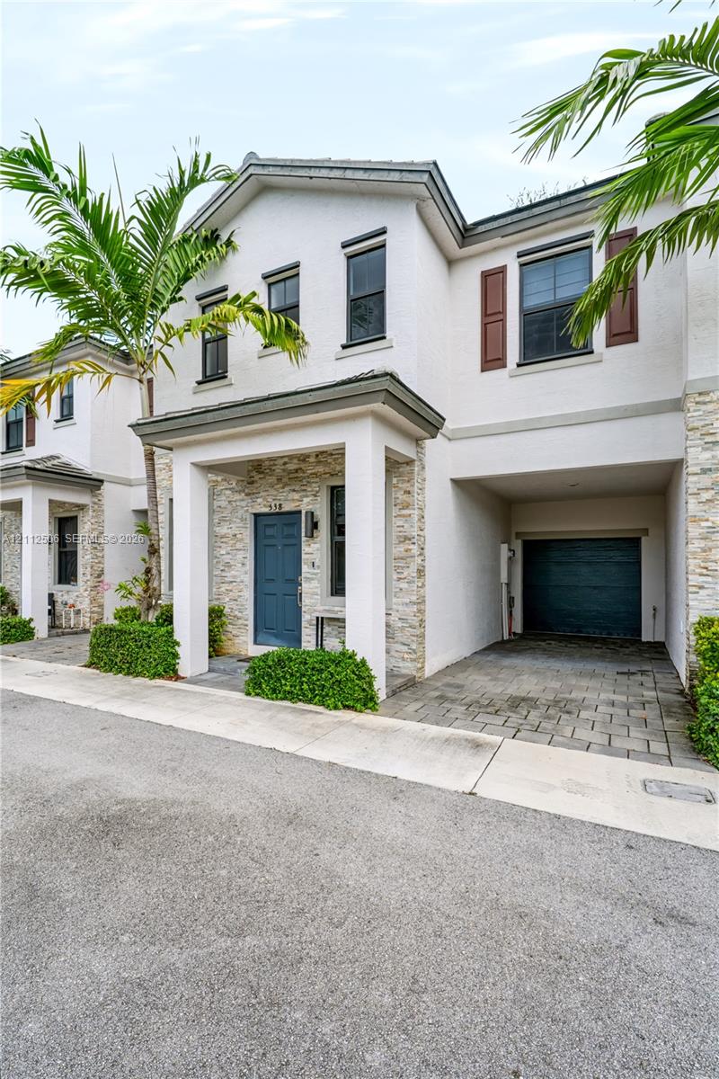 Stucco exterior featuring stacked stone veneer accents, covered entryway, paver driveway, and an integrated garage