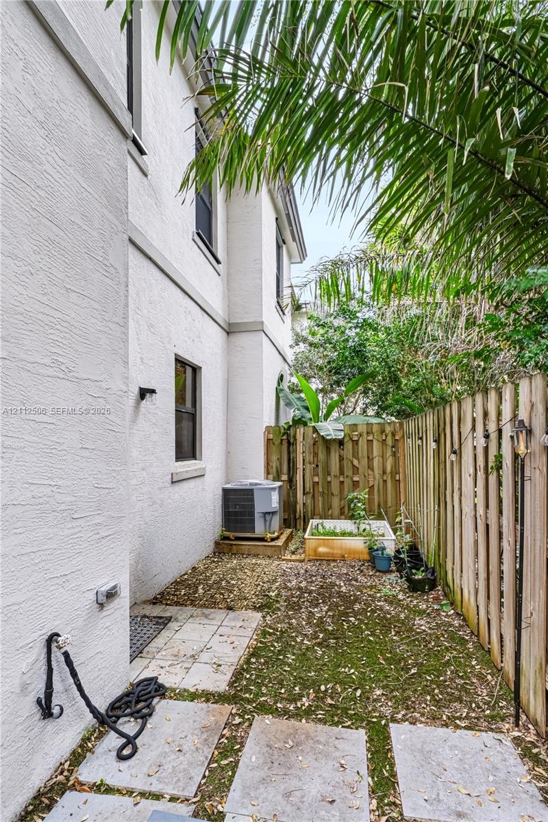 Stucco exterior side yard featuring concrete paver stones, a wooden privacy fence, and native landscaping