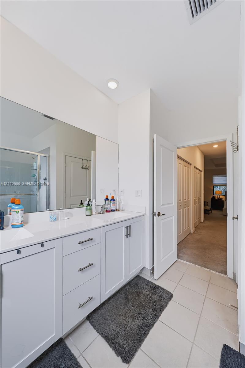 Bathroom featuring a dual-sink vanity with white cabinetry, solid-surface countertops, polished chrome fixtures, and a large-format vanity mirror
