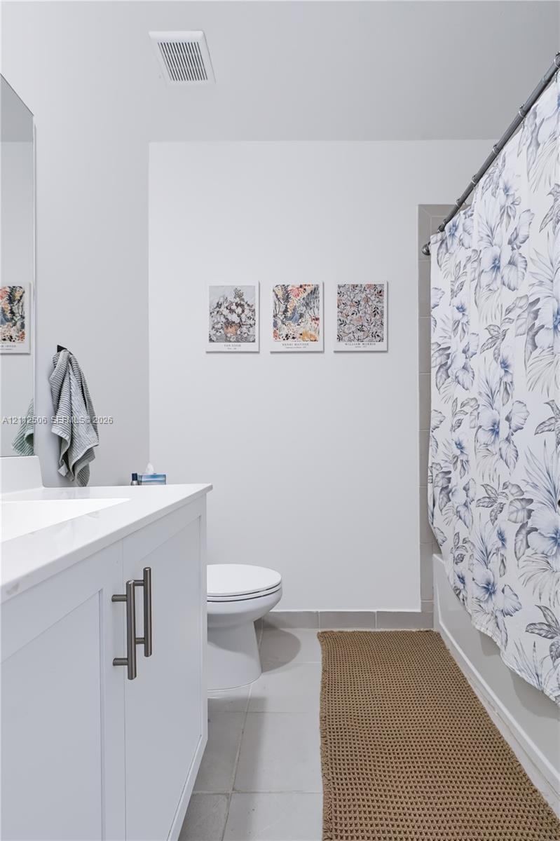 Bathroom featuring a white vanity cabinet with a stone-finish countertop, an integrated rectangular sink, dual-handle hardware, and a tub-shower combination with ceramic tile surround