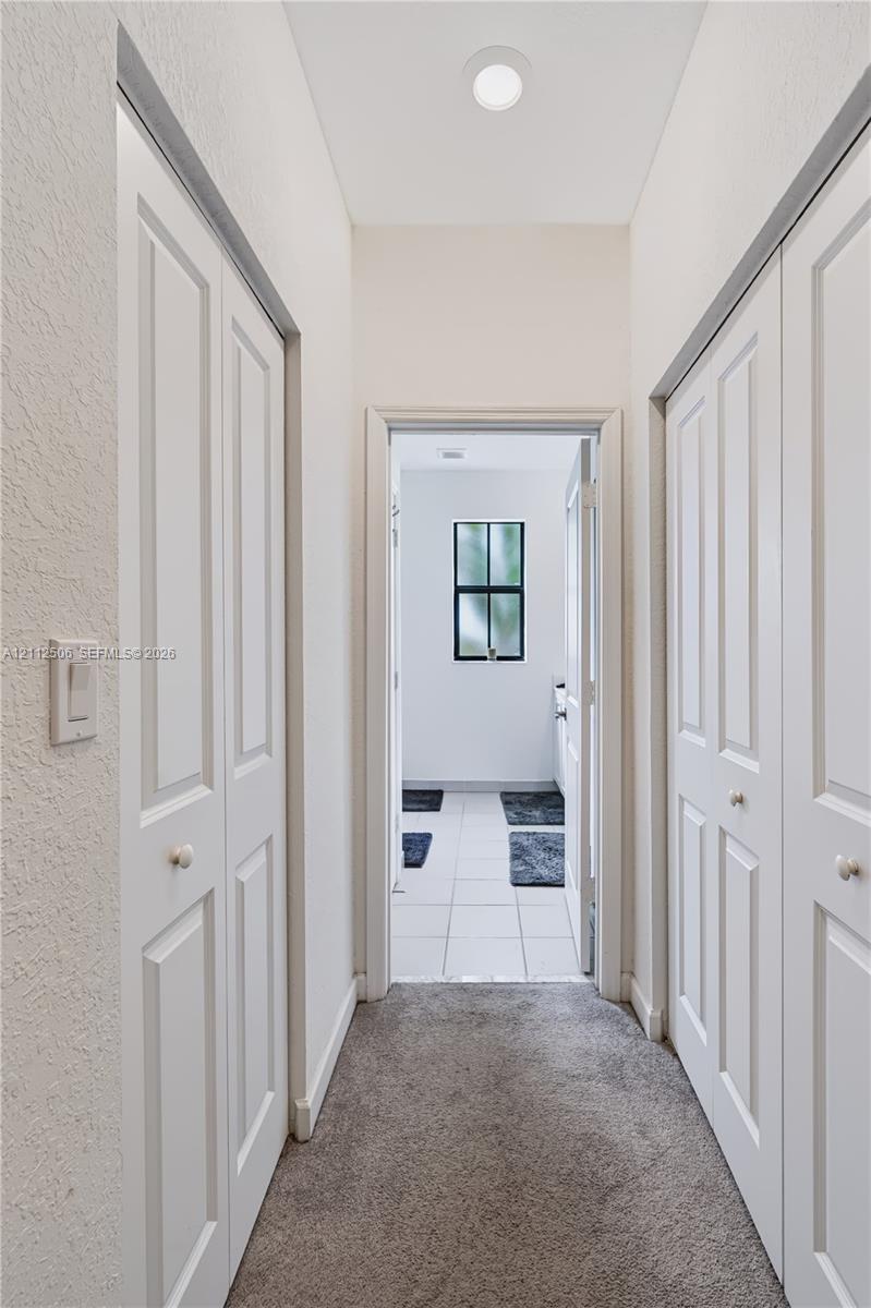 Hallway featuring neutral carpeting, dual white paneled bifold closets, and recessed ceiling lighting