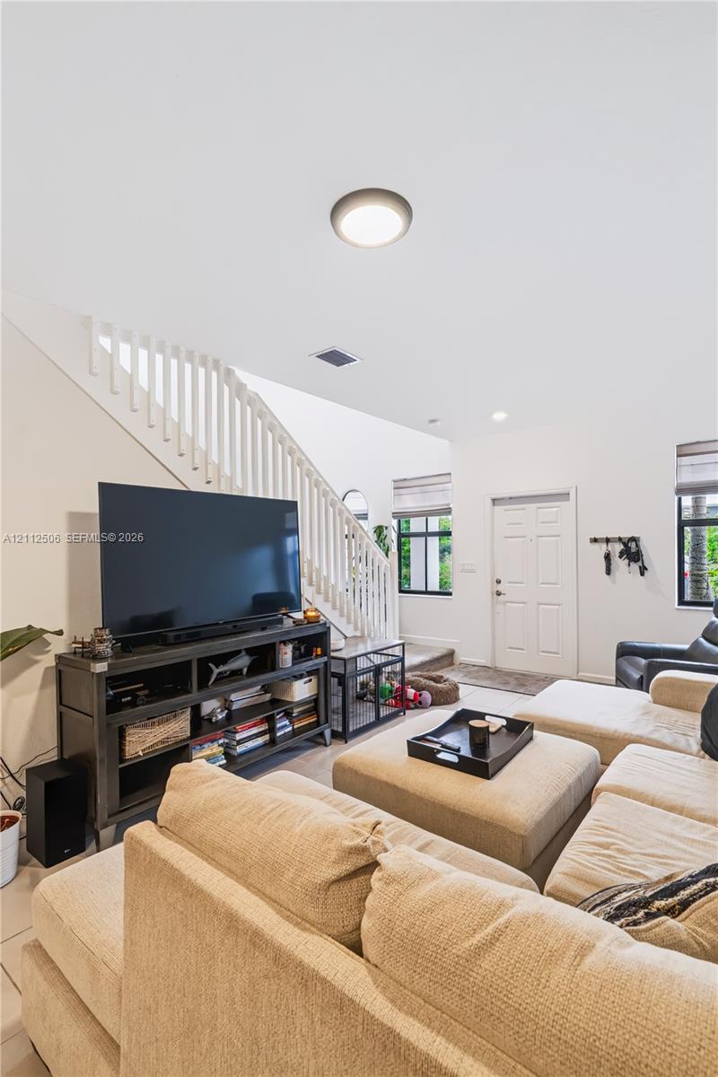 Open-concept interior featuring high ceilings, wood-finish flooring, a white staircase with a wooden handrail, and windows with integrated blinds