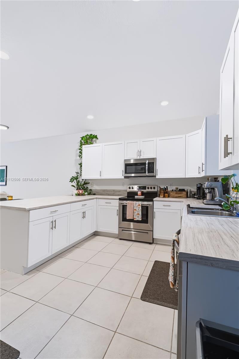 Kitchen featuring white shaker-style cabinetry, stainless steel appliances, light-toned countertop surfaces, and large-format tile flooring