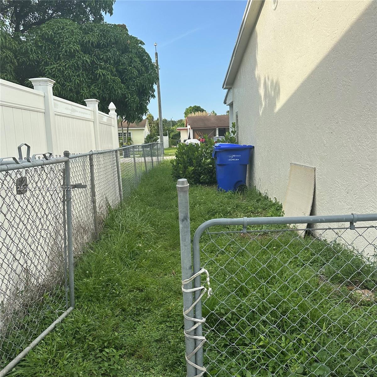 Exterior side yard area featuring a stucco wall finish, white vinyl privacy fencing, and chain-link metal fencing