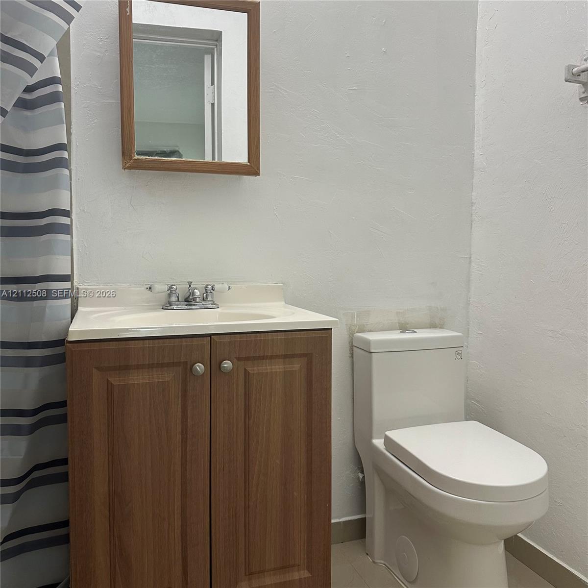 Bathroom featuring a wood-finish vanity cabinet, integrated sink with a chrome dual-handle faucet, rectangular wood-framed wall mirror, and a white one-piece toilet