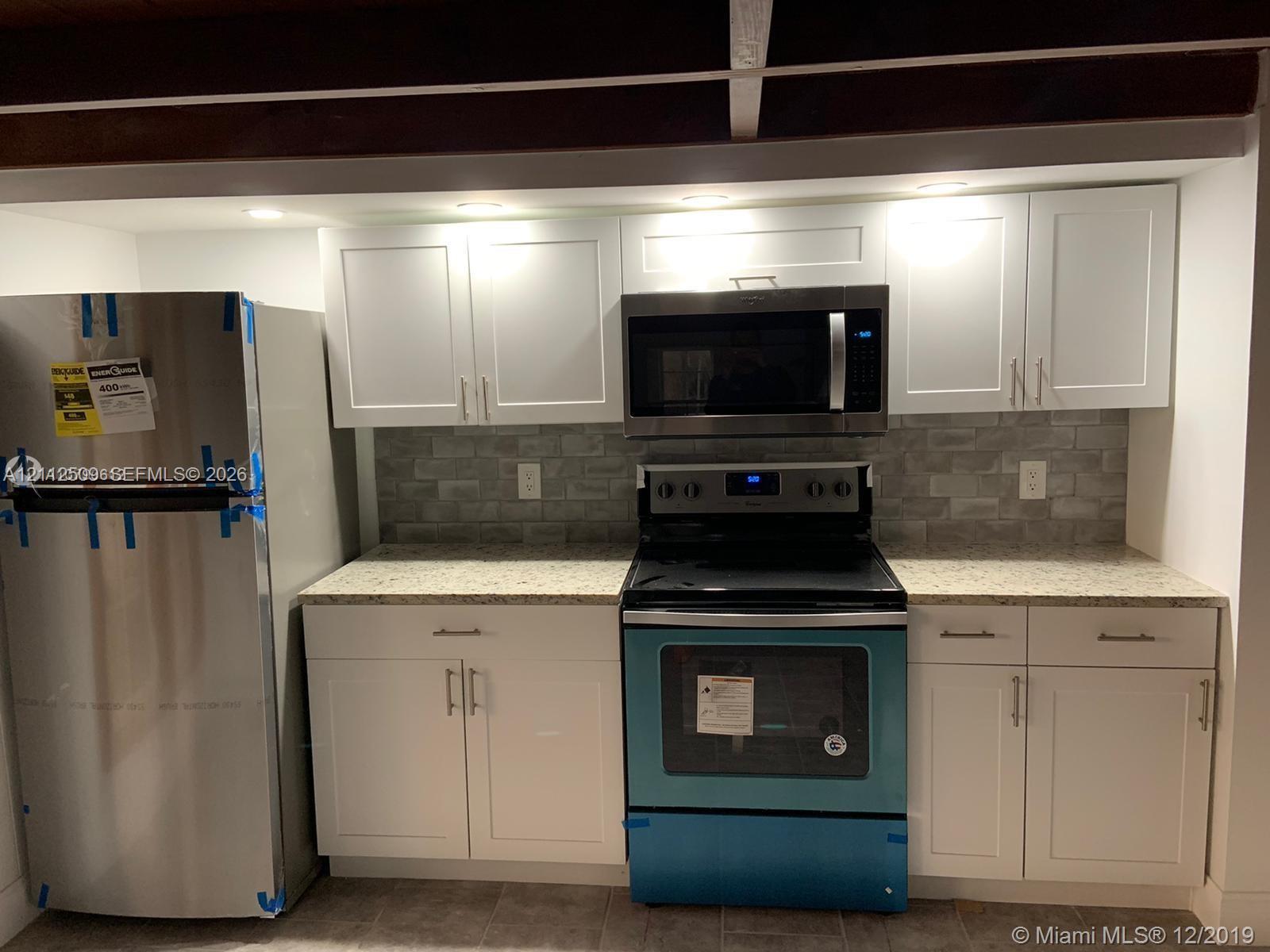 Kitchen featuring white shaker-style cabinetry, stone-finish countertops, stainless steel appliances, and a gray tile backsplash