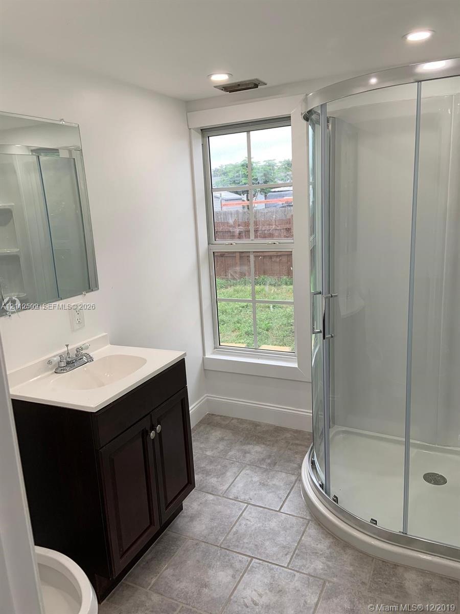 Bathroom featuring a dark wood-finish vanity, light-toned countertop with an integrated sink, curved glass-enclosed shower, and tile flooring