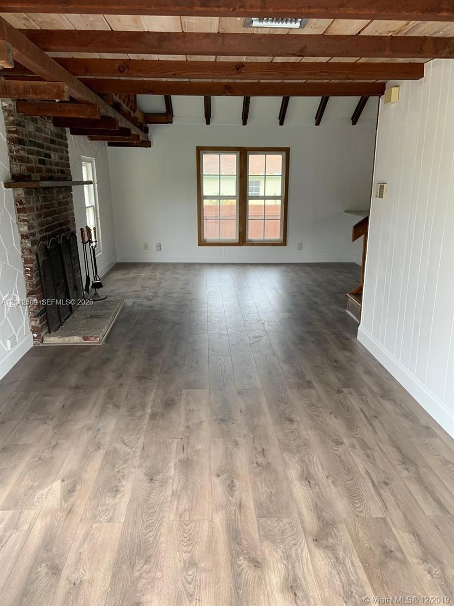 Exposed wood ceiling beams, floor-to-ceiling brick fireplace with a stone hearth, and wood-finish flooring