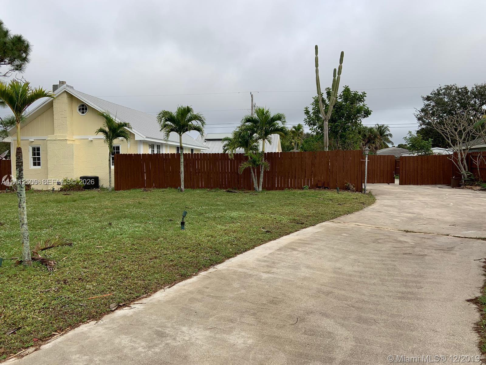 Exterior featuring pale yellow siding, a concrete driveway, a wood-slat privacy fence, and native palm landscaping