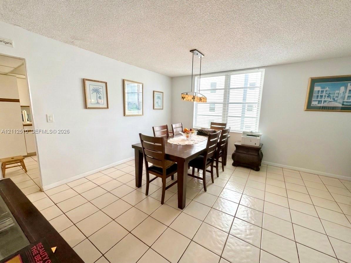 Spacious area featuring light-toned ceramic tile flooring, horizontal window blinds, and a multi-light metal pendant fixture