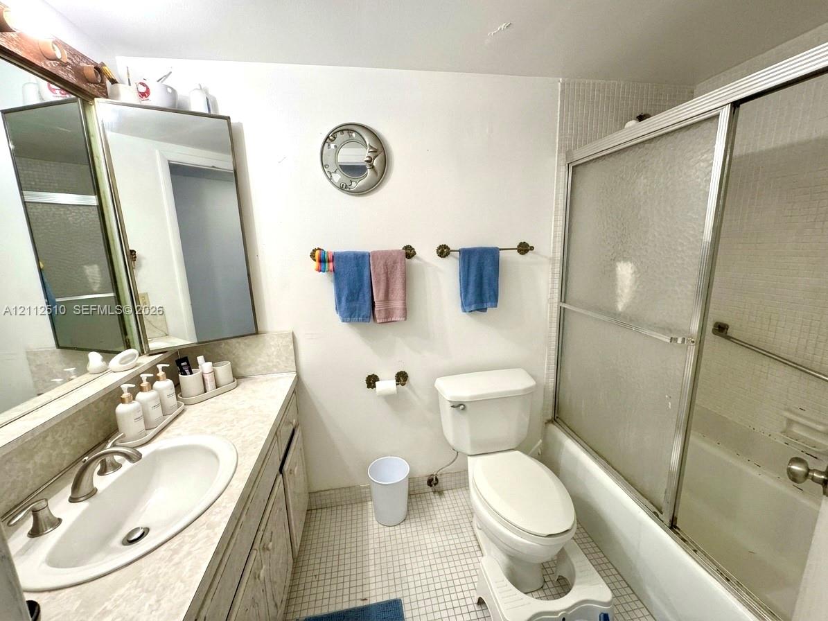 Bathroom featuring a vanity with an integrated oval sink, countertop, tri-panel mirrored cabinet, mosaic tile flooring, and a tub-shower combination with sliding glass doors