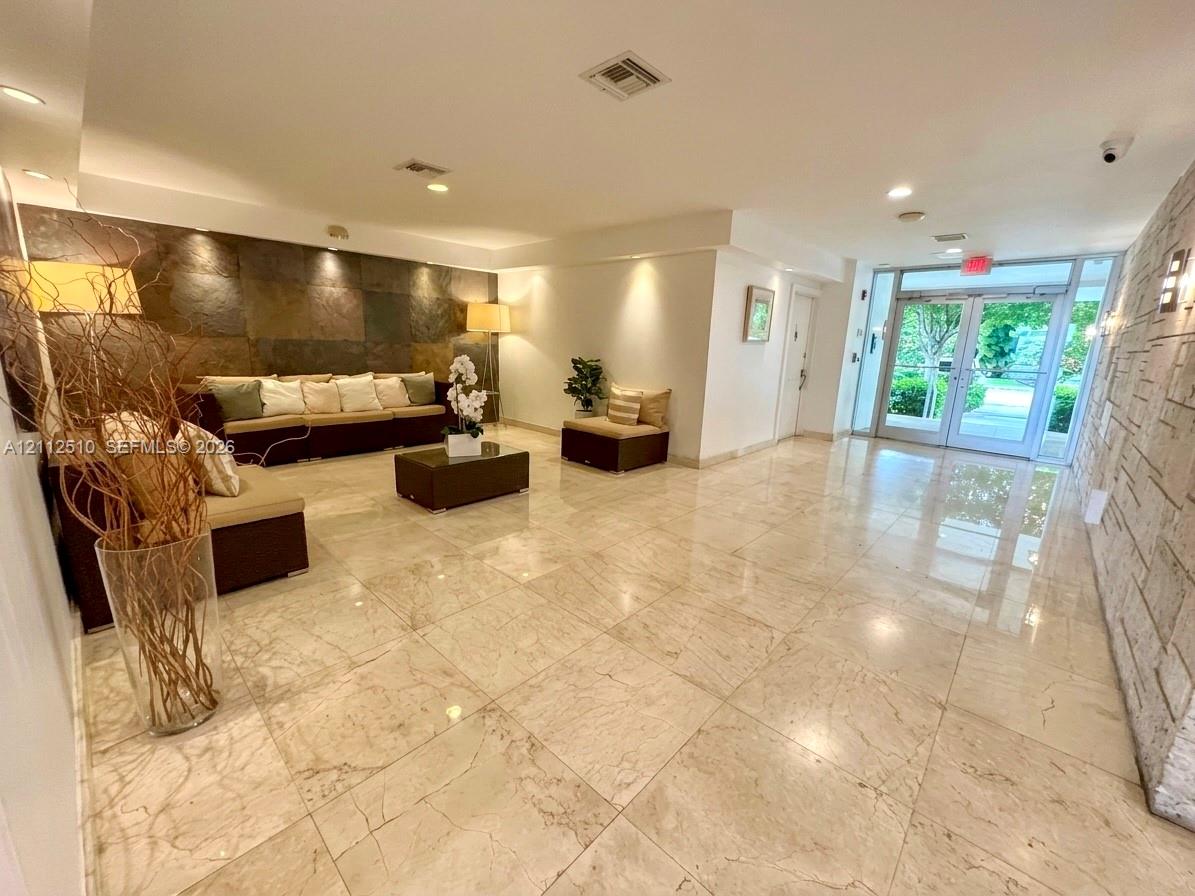 Lobby featuring polished stone flooring, large-format dark stone accent wall, light-toned stone textured wall, recessed lighting, and glass-paneled double entrance doors