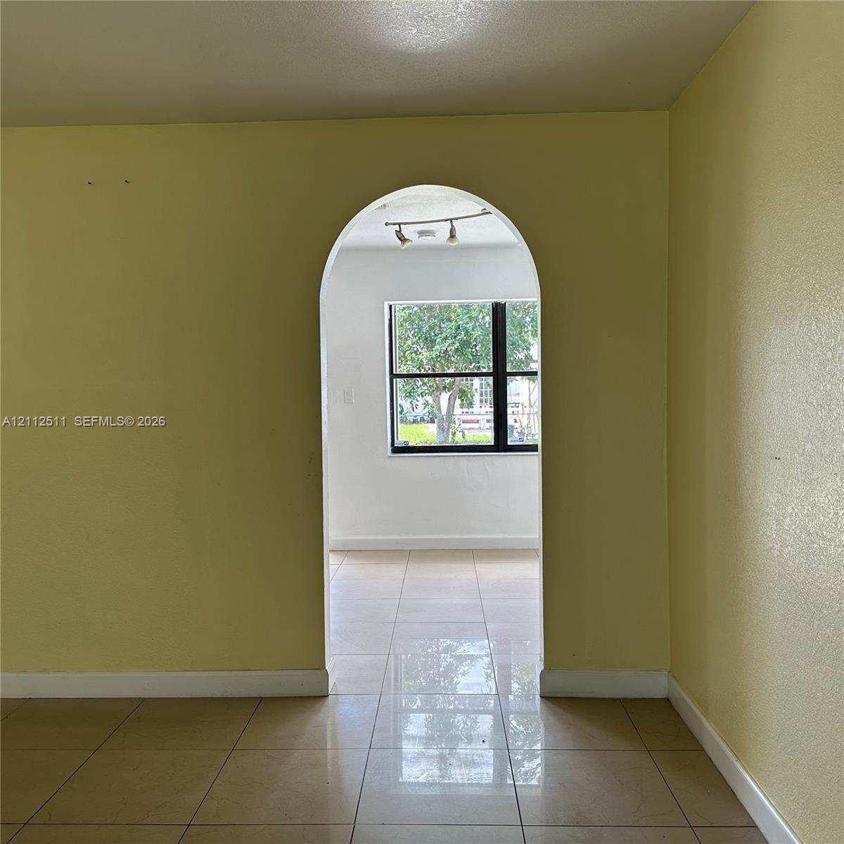 Architectural arched doorway with large-format tile flooring, multi-light track lighting, and a prominent window