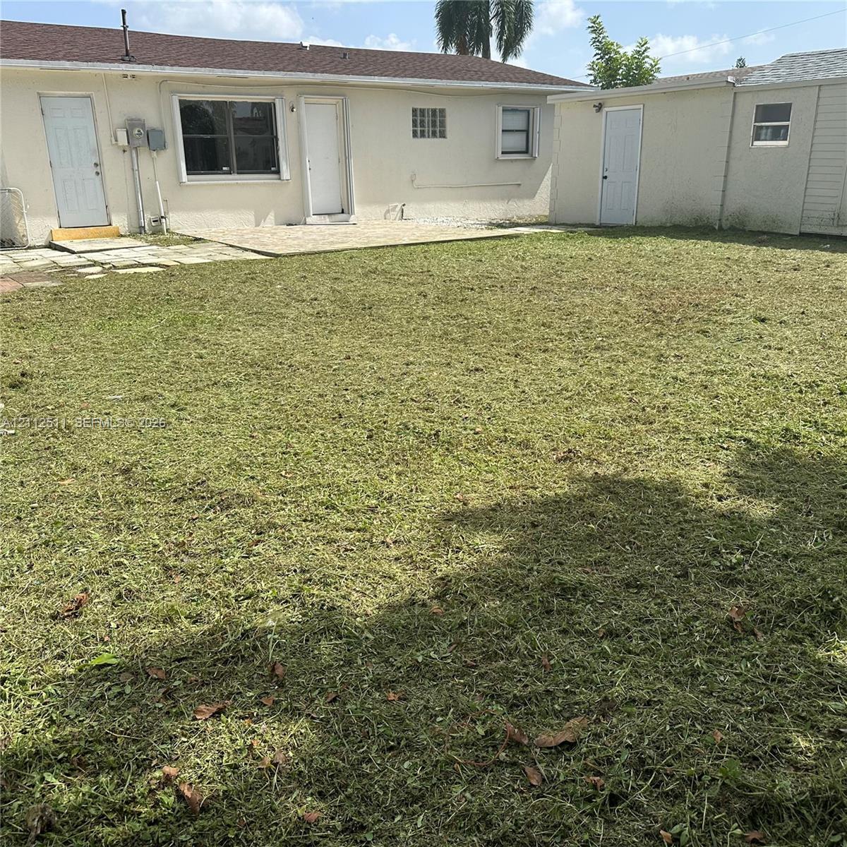 Expansive backyard featuring a concrete patio, detached storage structure, and stucco exterior walls