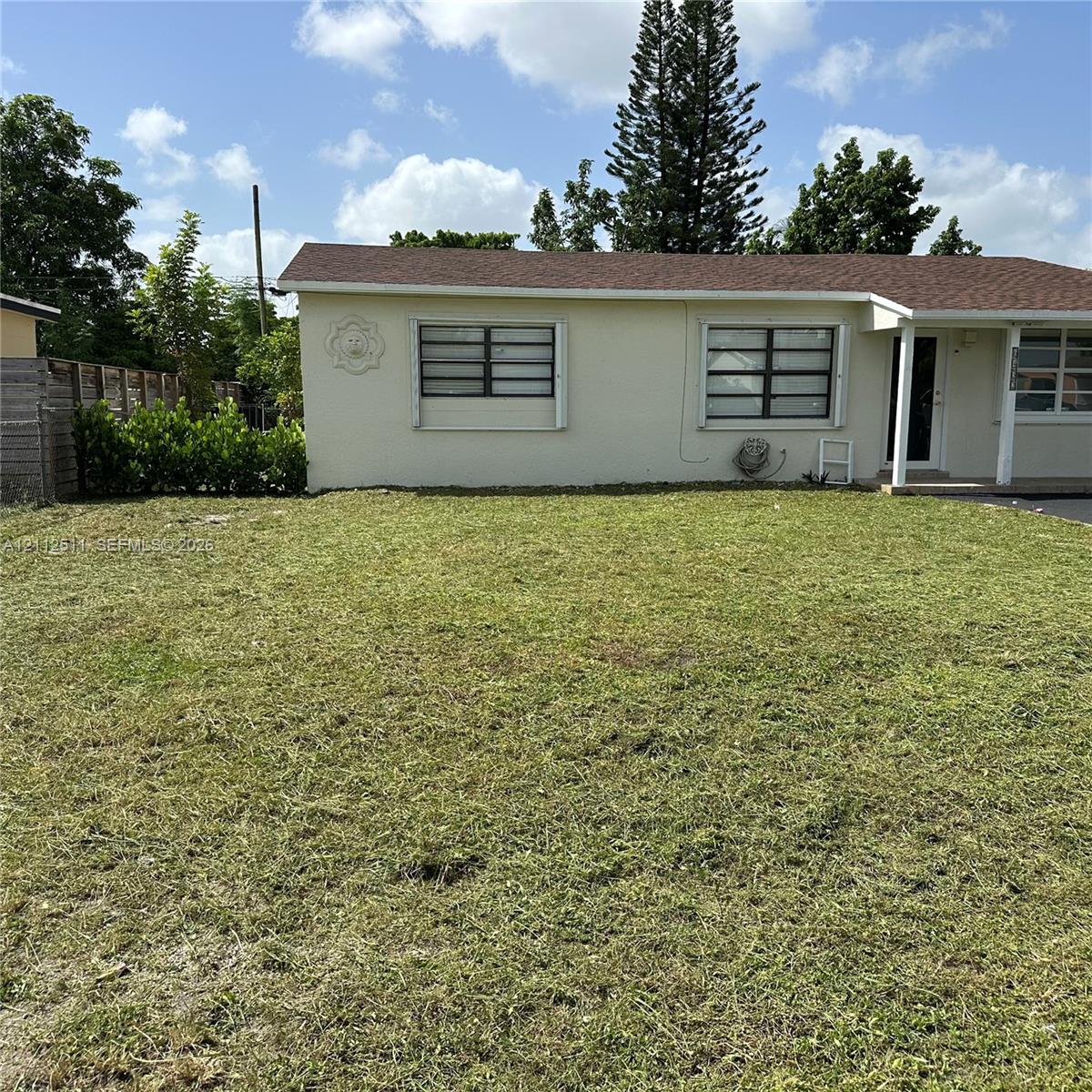 Single-story exterior featuring a light-colored stucco facade, shingled roof, aluminum-framed windows, and an expansive lawn