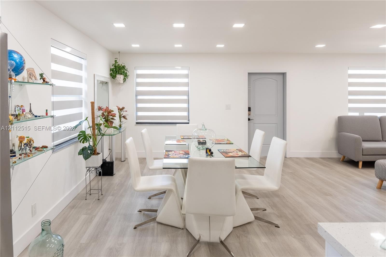 Neutral-toned wood-finish flooring, recessed lighting, banded roller shades, and integrated glass shelving
